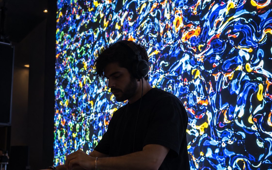 DJ pinchando en cabina delante de una pantalla con visuales de colores