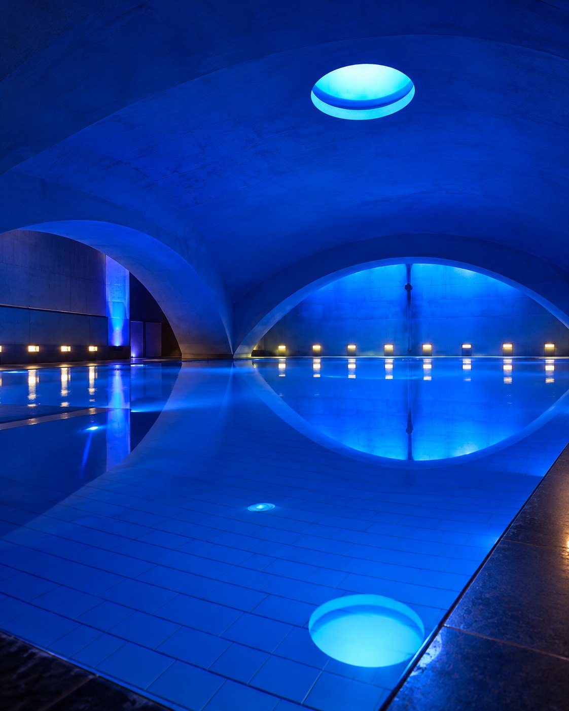 Piscina de Liquidrom bajo la cúpula de hormigón, iluminada en azul y con el tragaluz del techo reflejado en el agua
